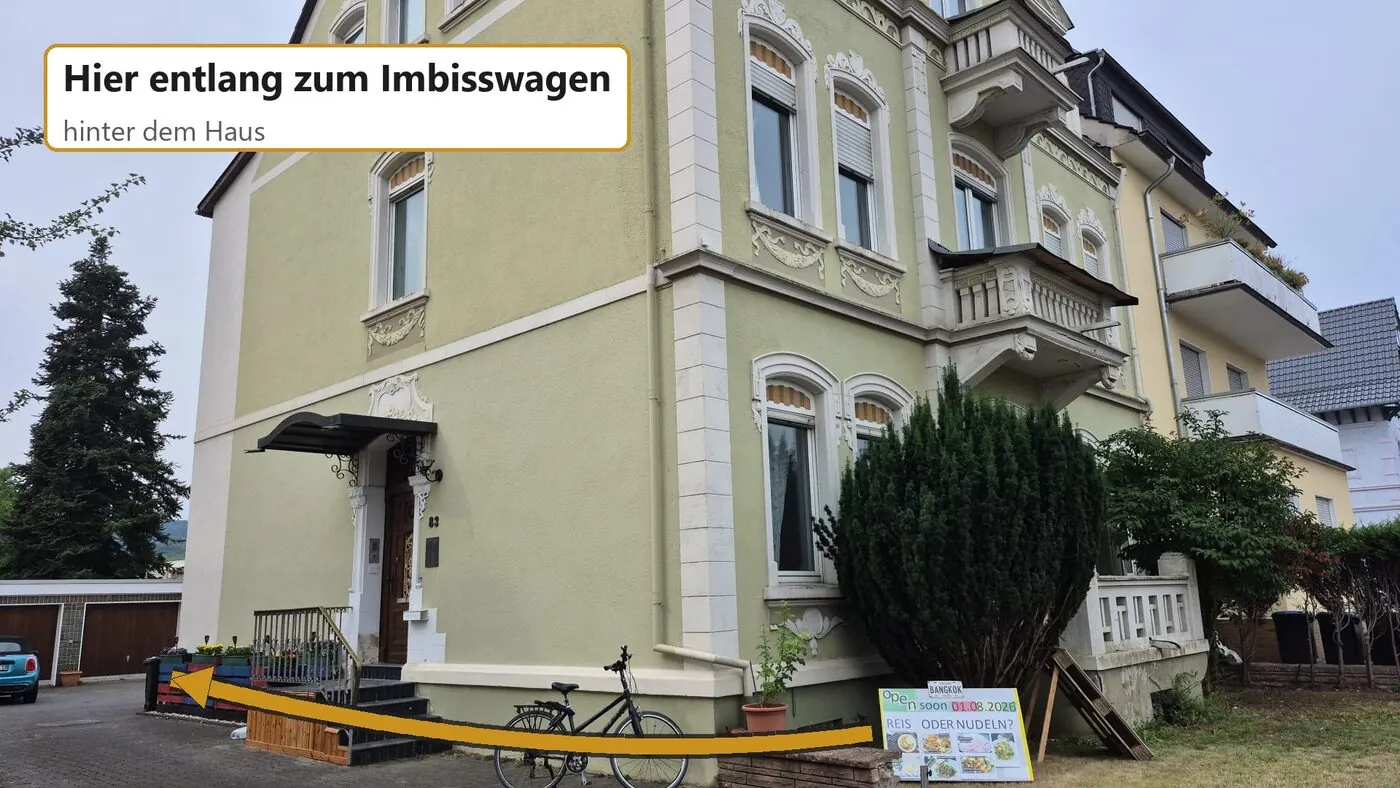 Das Haus Wilhelmstraße 83 von der Straße aus. Ein Pfeil weist links am Haus vorbei in die Einfahrt, hinter der der Imbisswagen steht.